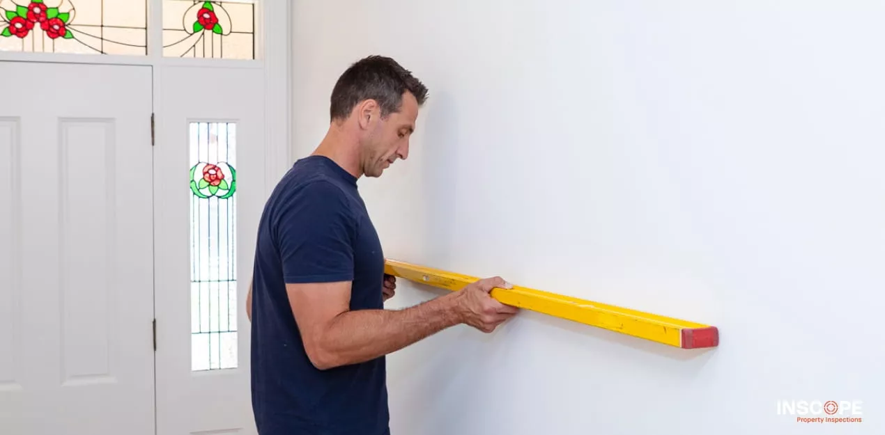 Building inspector using a spirit level to assess wall alignment during a residential property inspection.